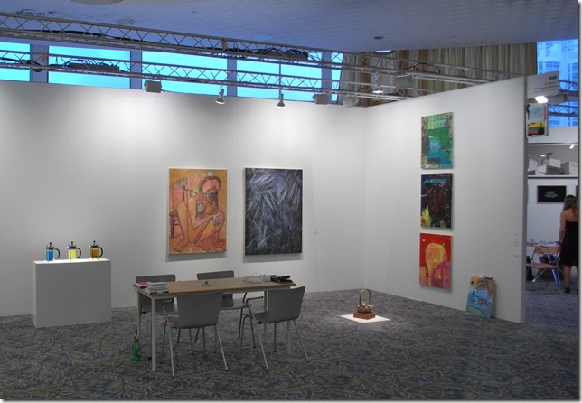 The Green Gallery of Wisconsin shared a large booth with New York City’s 47 Canal.  From left, the three colored coffee presses, the large Picasso-esque style painting, and the black-and-blue abstract are all by Scott Reeder. The three works on the wall on the right are by Tyson Reeder, as is the small one leaning against the wall. The small bronze basket sitting on two bricks on the riser on the ground is by Amy Yao. (Courtesy The Green Gallery)